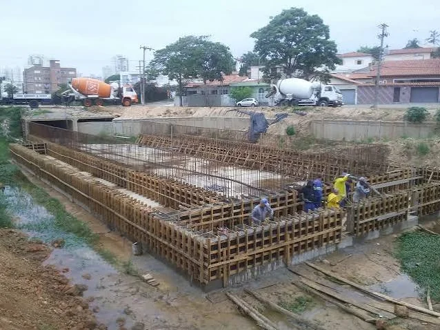 Fôrmas e armaduras de fundação com caminhões betoneira ao fundo
